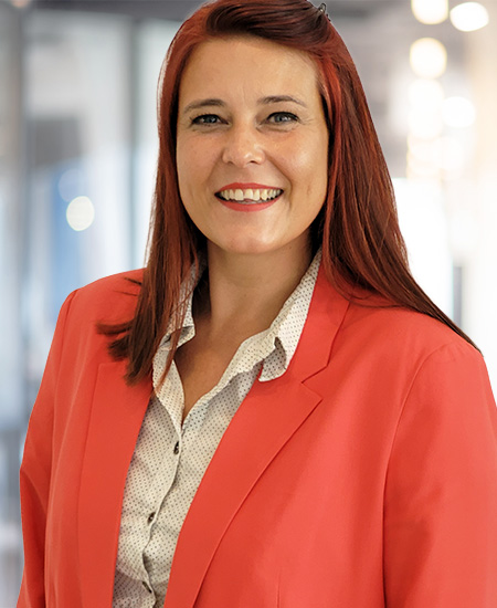 Eine lächelnde Frau in einem roten Blazer vor einem unscharfen Hintergrund.