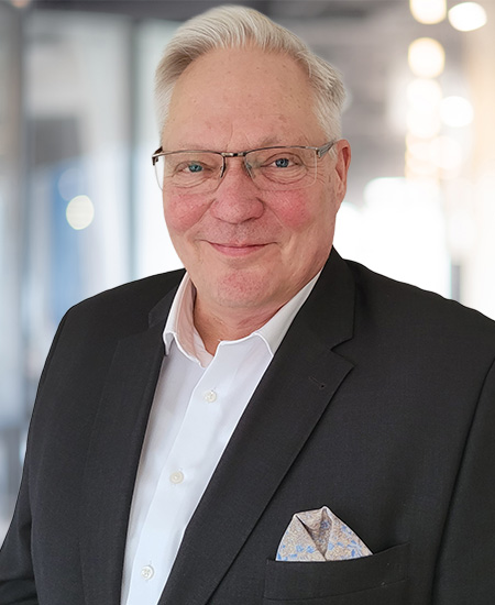 Ein älterer Herr mit weißem Haar lächelt freundlich im dunklen Anzug und weißem Hemd