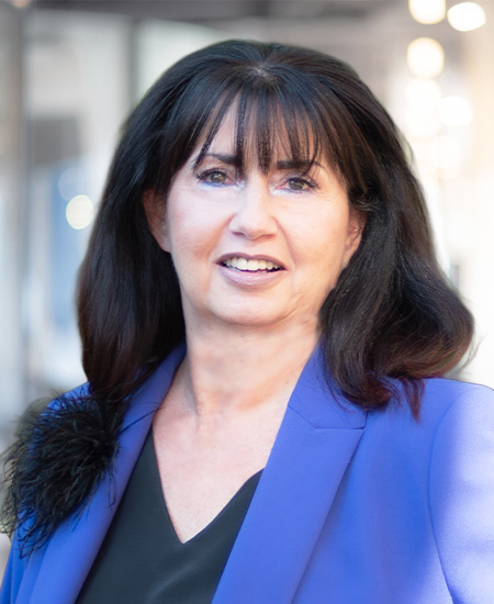 Eine Frau mit langen, dunklen Haaren lächelt freundlich in einem blauen Blazer