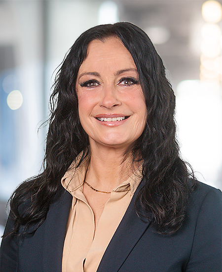 Eine Frau mit langen dunklen Haaren lächelt freundlich in einem Business Outfit